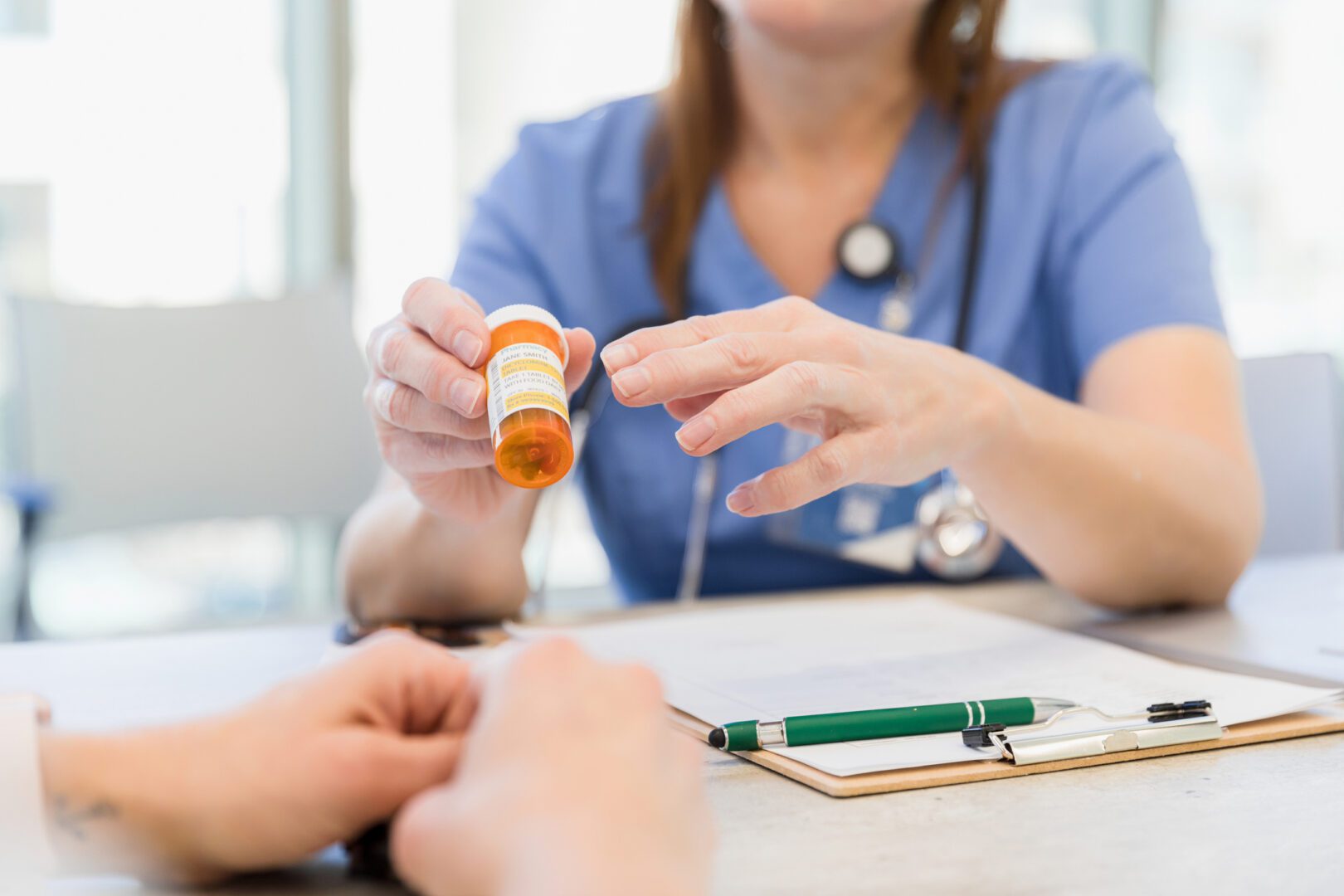 The focus of the photo is on the bottle of prescription medication held by the unrecognizable female doctor as she explains the side effects to the unrecognizable female patient.
