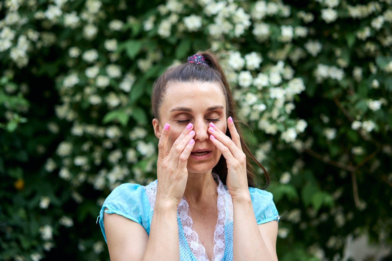 Woman rubbing eyes near blooming tree in spring time. Itchy eyes from allergy.