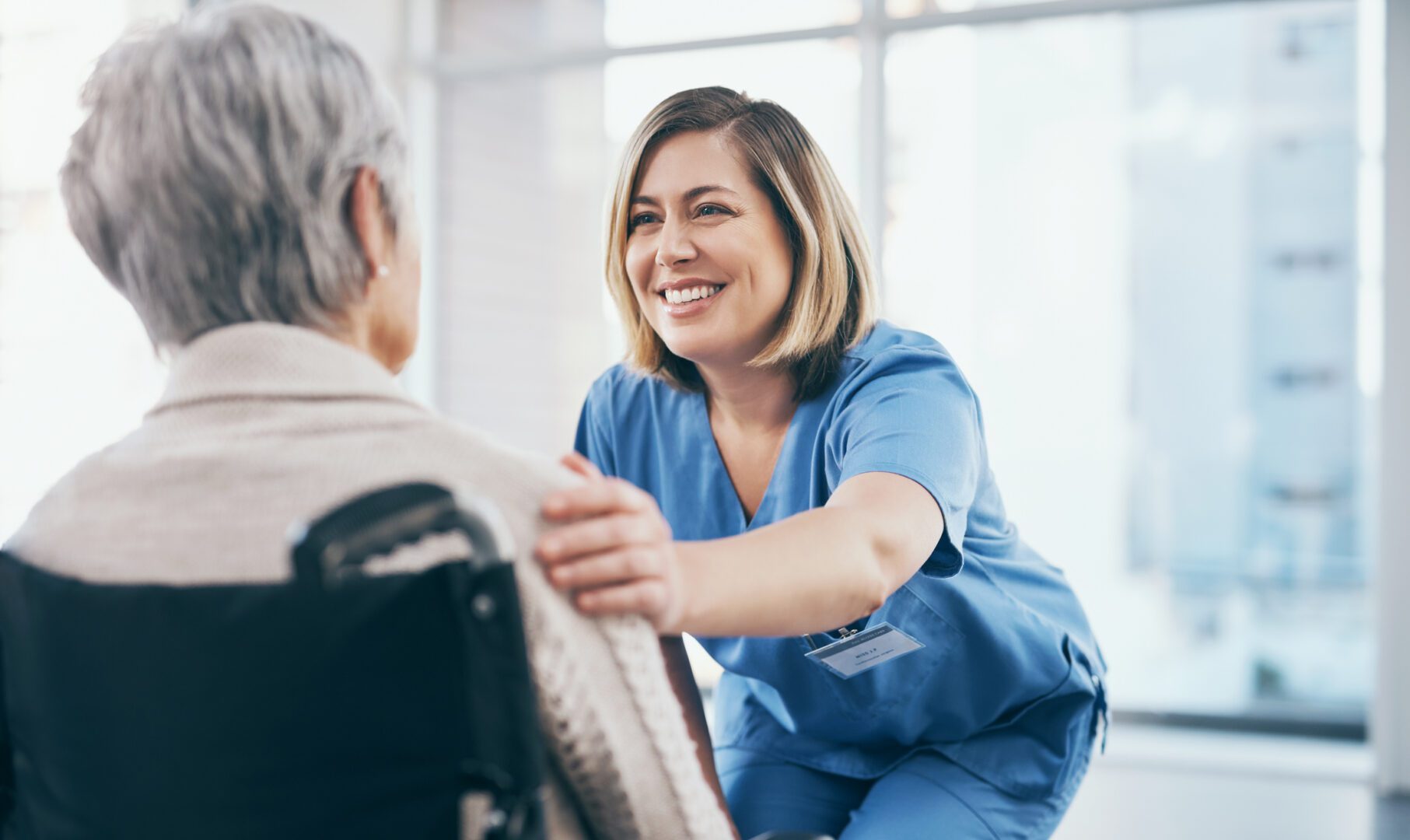 Nurse or caregiver taking care of a senior retired woman sitting on a wheelchair in a modern facility. Happy female healthcare professional consulting a mature lady and giving support