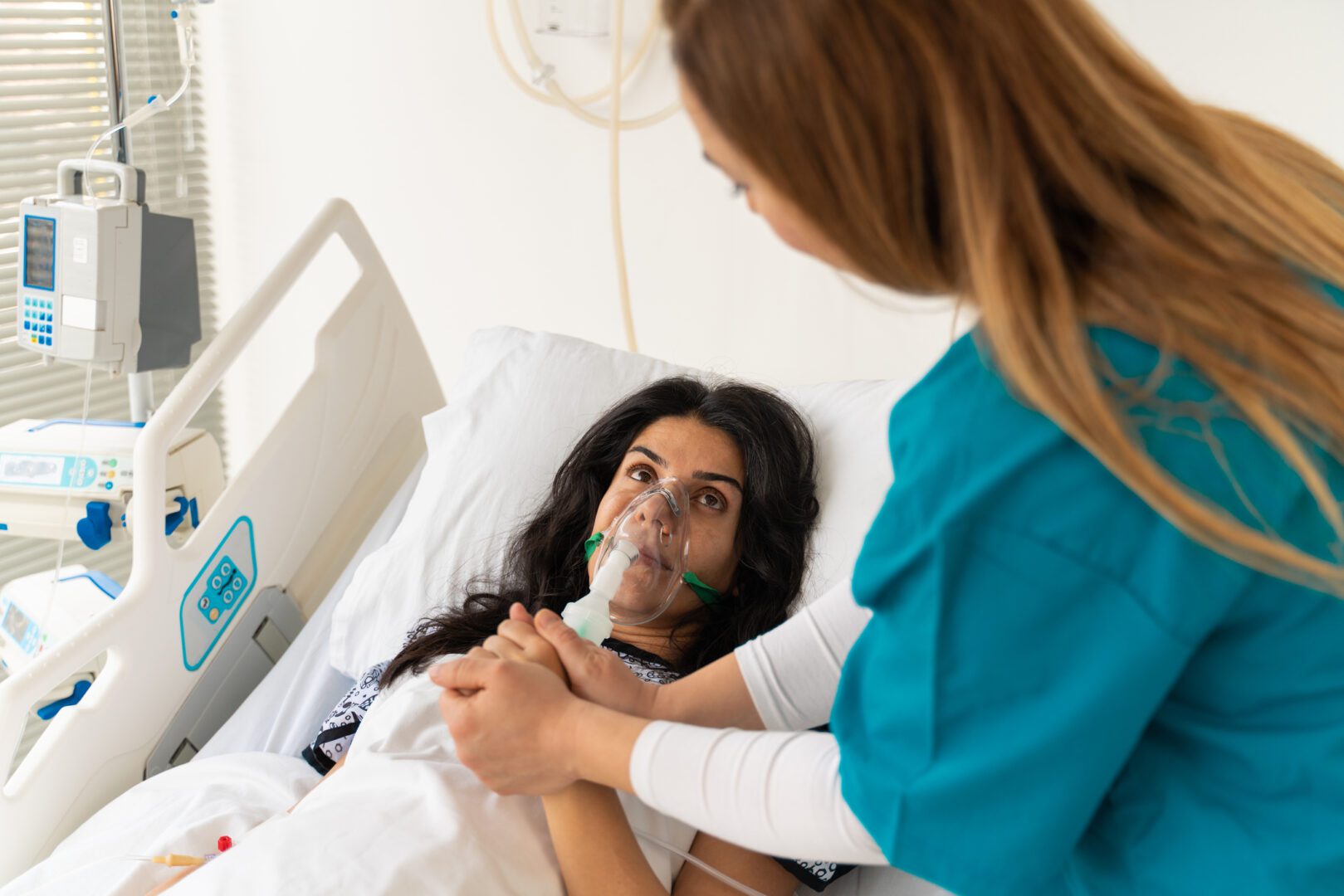 Portrait of woman lying in hospital bed with oxygen mask and holding hands with caring doctor or nurse