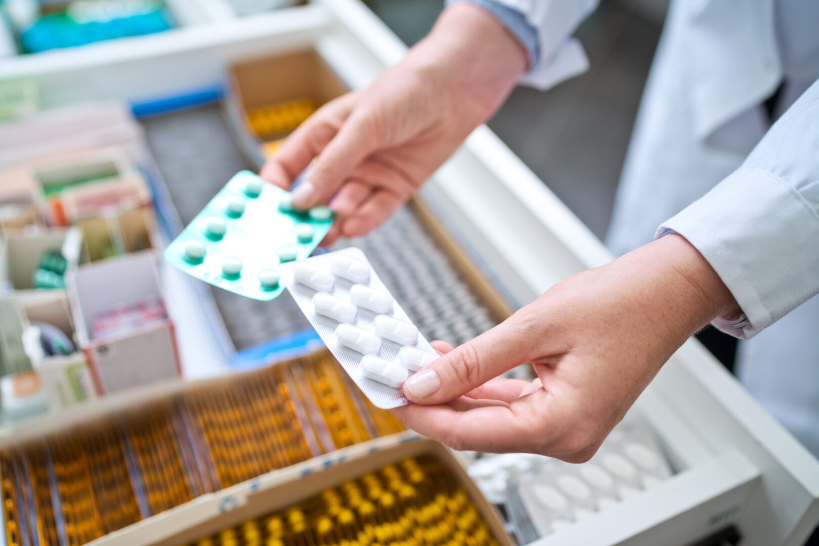 Pharmacists holding pills in hands above drawer with medicines. Close up of hands, unrecognizable person.
