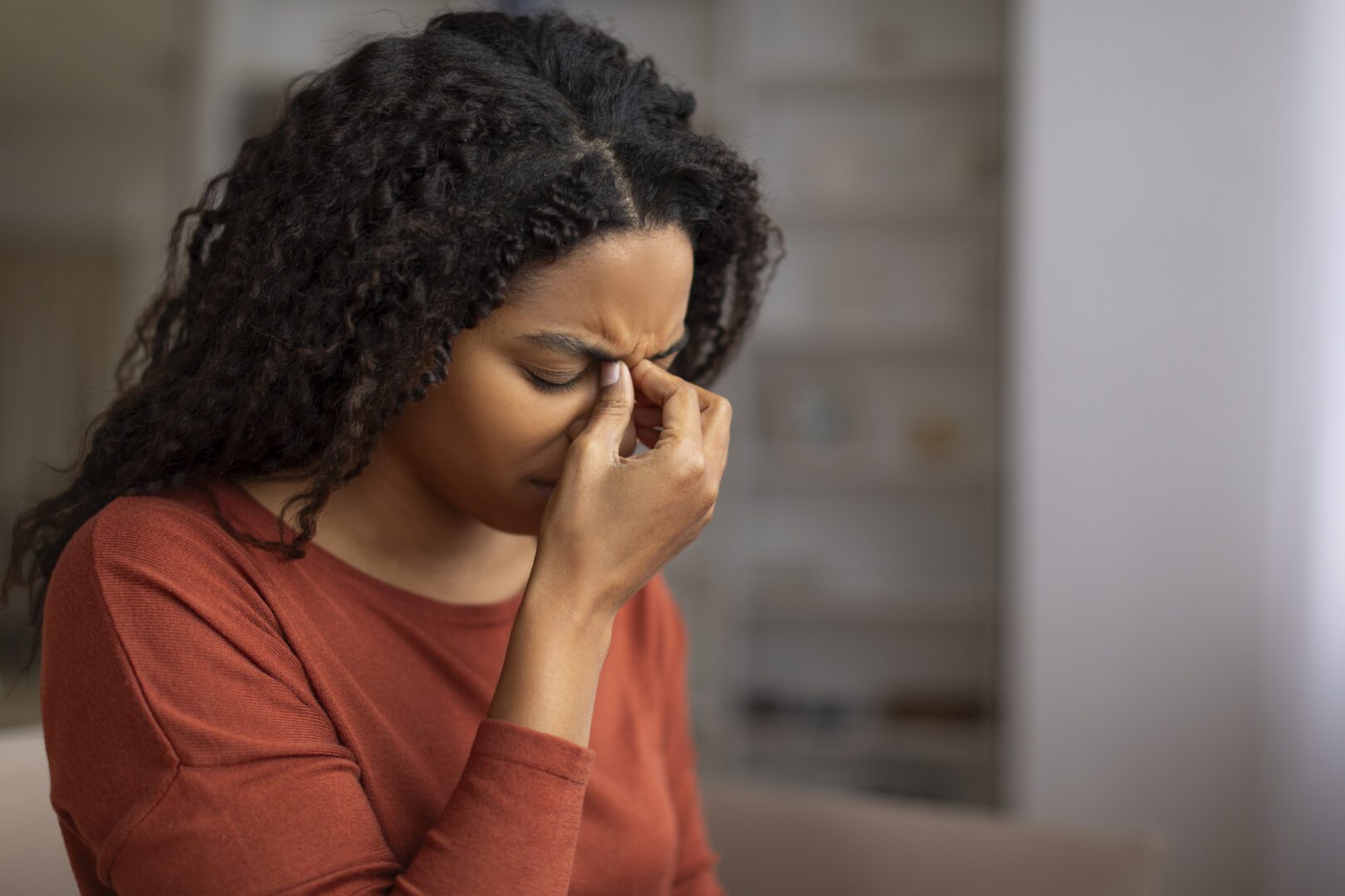 Young black woman feeling sinus pain, pressing on the bridge of her nose, sick african american woman closing eyes and frowning, showing signs of discomfort or headache at home, closeup