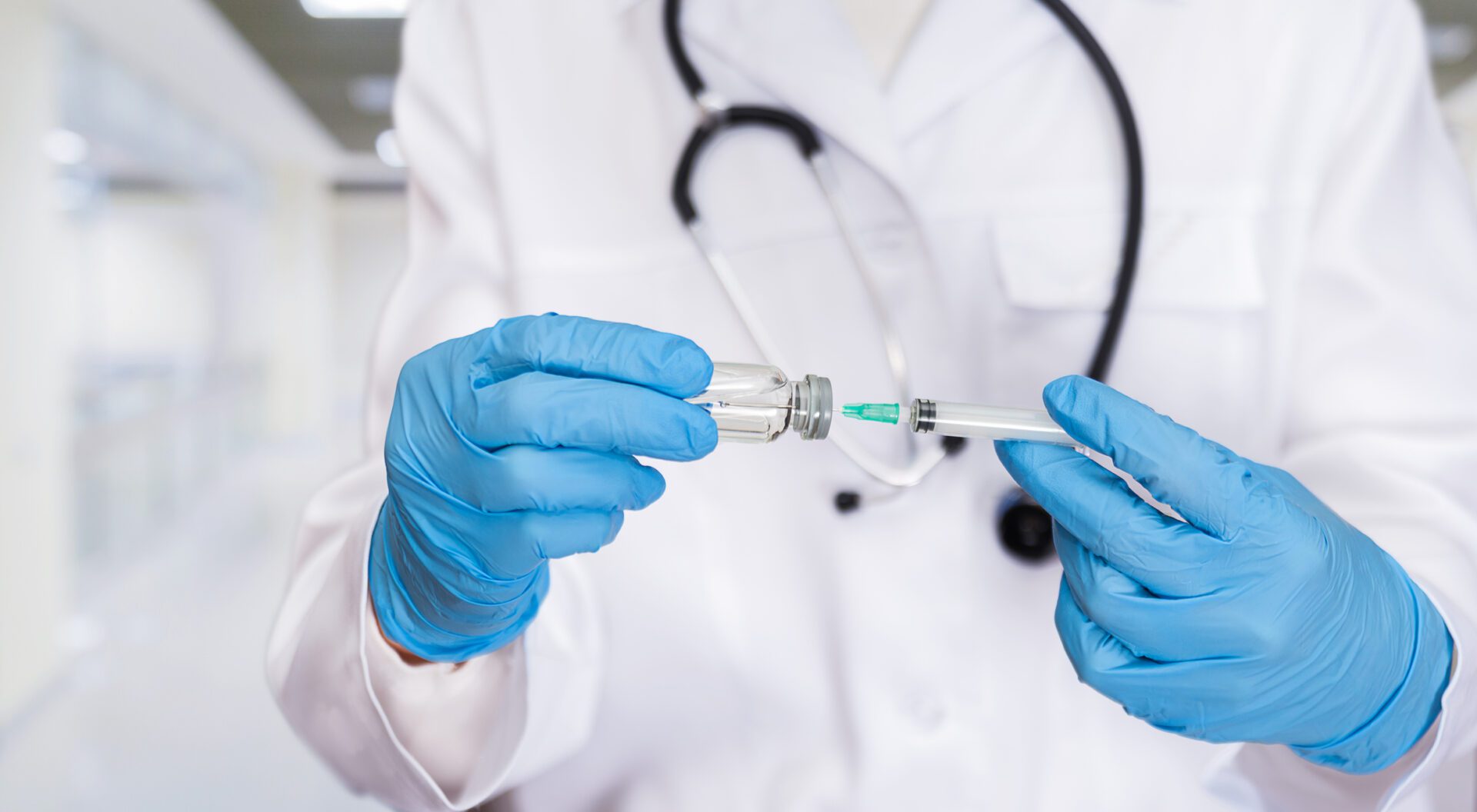 A skilled healthcare worker in gloves is drawing vaccine fluid into a syringe in a well-lit clinic.