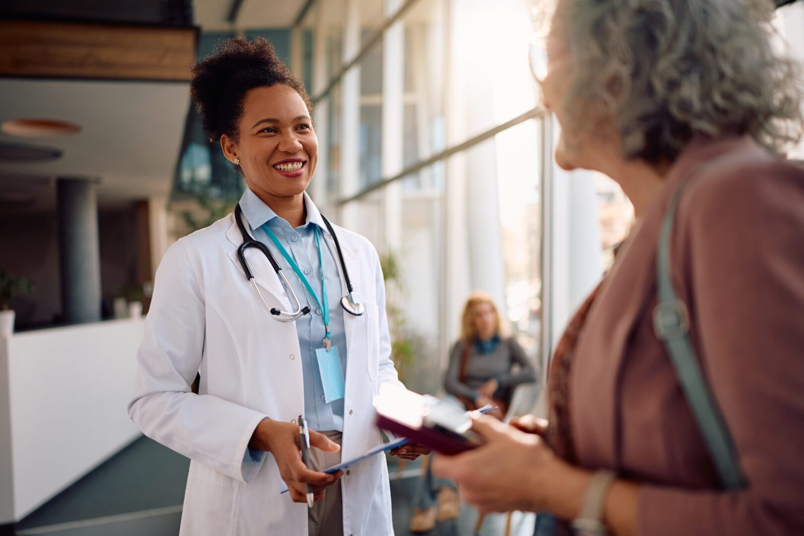 Happy African American doctor and her senior patient communicating during medical appointment at clinic.