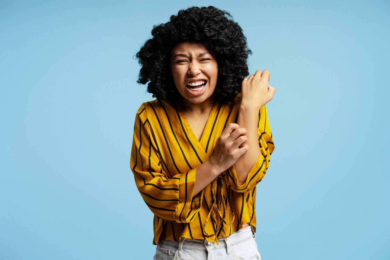 Young woman scratching her arm, experiencing intense allergy itching and discomfort, showcasing red, irritated skin in a studio setting