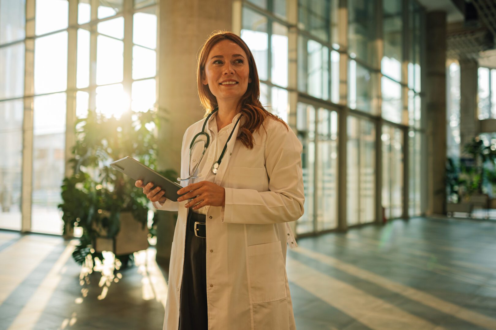 Confident doctor using a digital tablet, enjoying a fulfilling role in a modern hospital environment, radiating positivity and professionalism