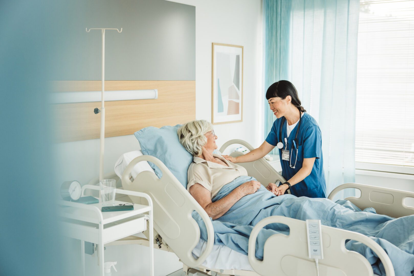 Nurse talking to senior woman in hospital bed. She is showing empathy for her condition.