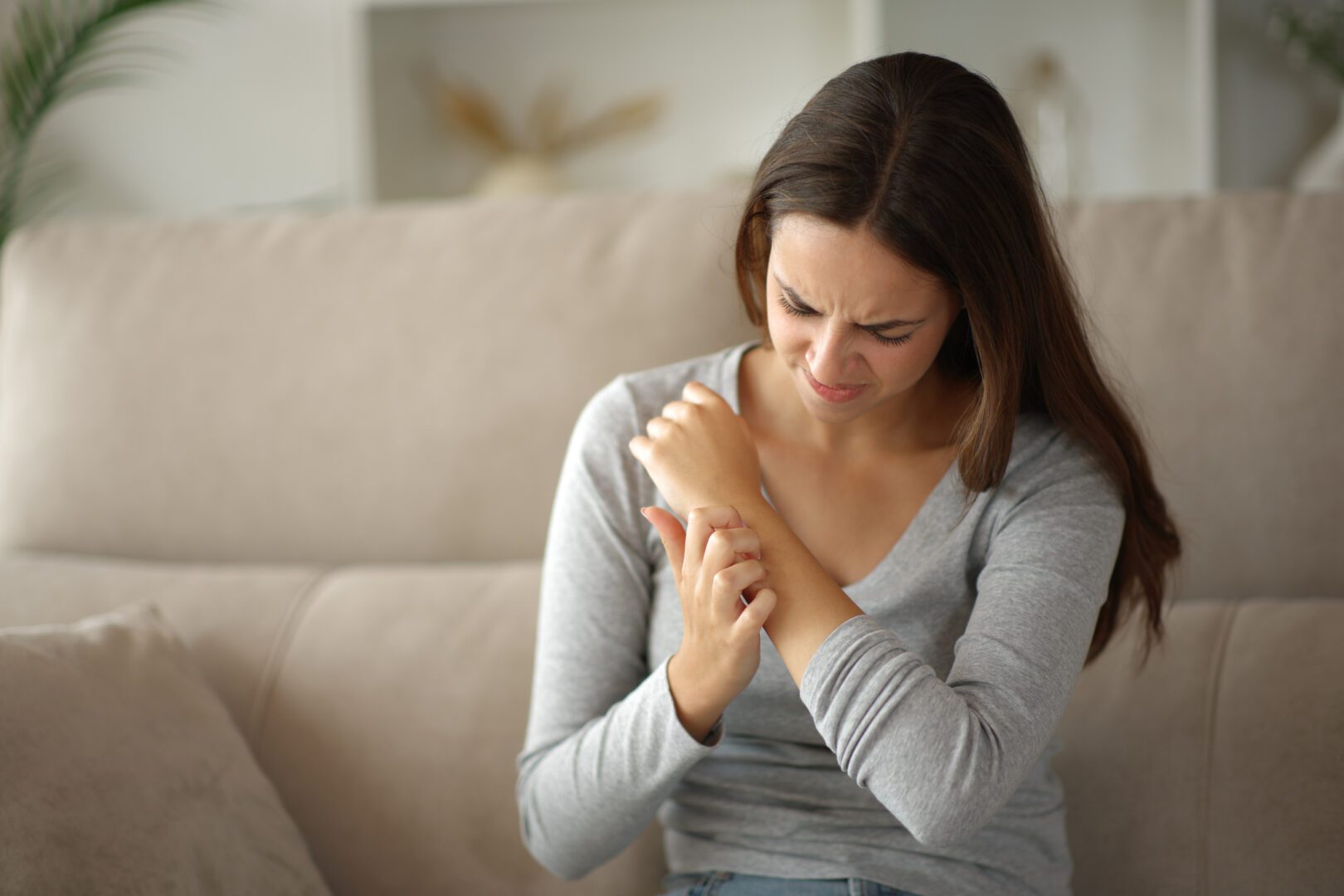 Woman rashing arm after insect bite sitting on a couch at home