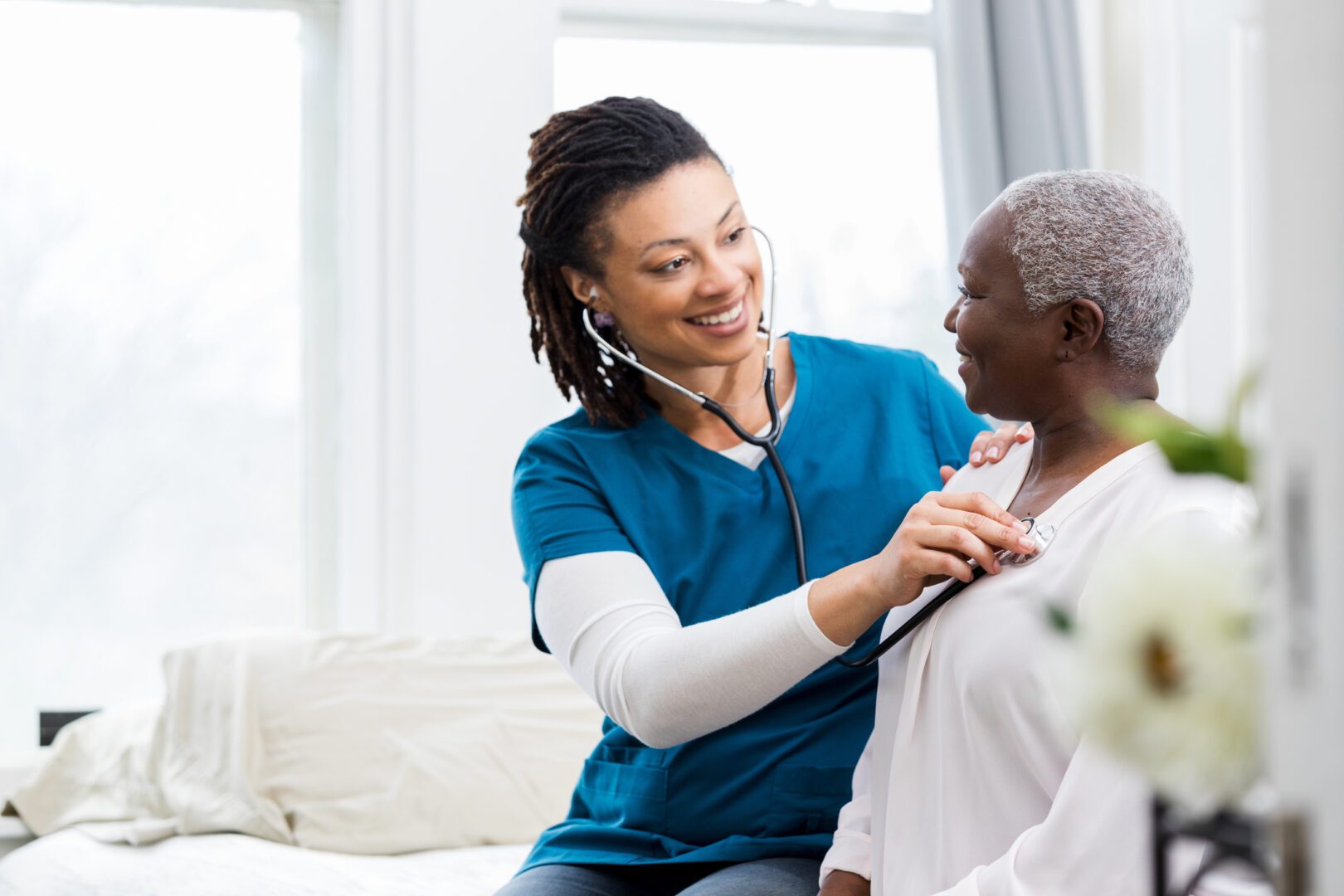A nurse attentively listens to a patient's chest with a stethoscope, both smiling.