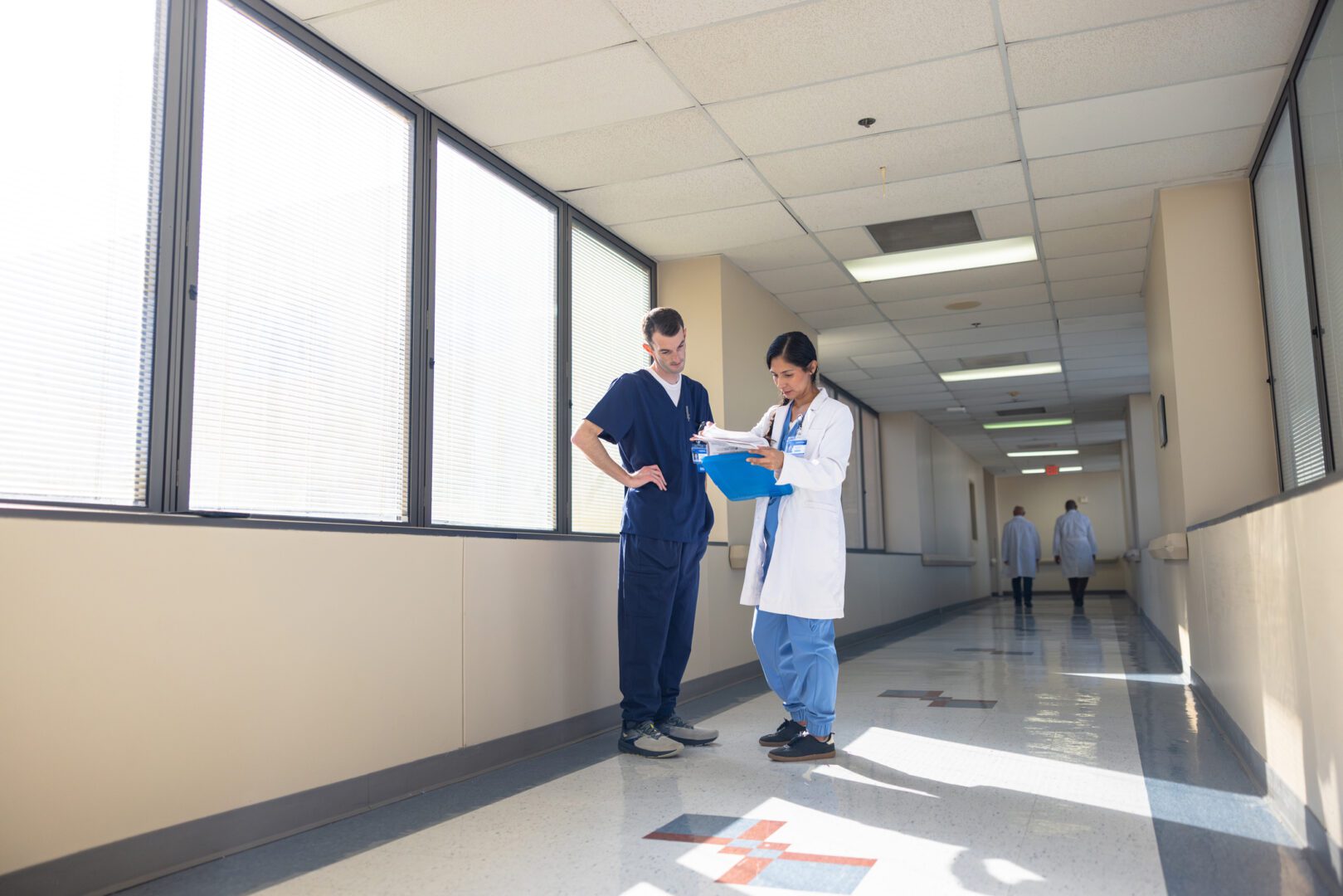 Female hispanic doctor looking over medical test results in a hospital hallway with a male nurse