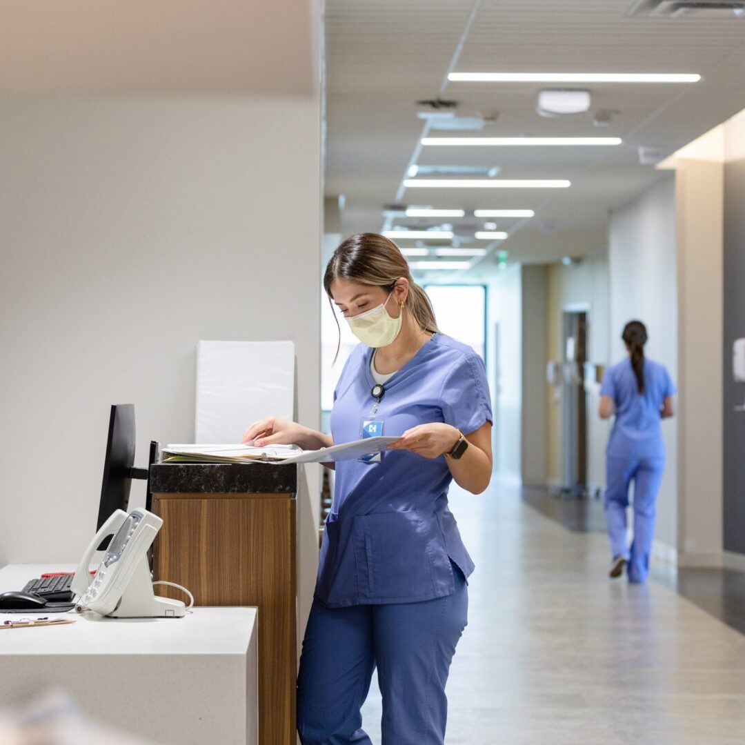 The nurse stands at the computer desk and reads a patient's medical record before consulting with the doctor.